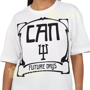 May include: White t-shirt featuring a black graphic design. The design includes the word "CAN" above a symbol and the words "FUTURE DAYS" in a banner. The shirt has short sleeves and a crew neck.