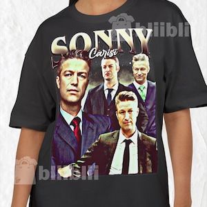May include: Black t-shirt featuring a vintage-style graphic of the word "SONNY" above a group of men in suits. The graphic includes the name "Carisi" and a faded, distressed effect, giving it a retro look.