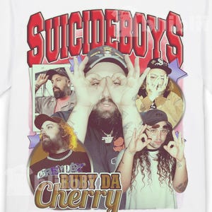 May include: White t-shirt featuring a graphic of the band Suicideboys. The design includes the band's name in red, a collage of the band members, and the text "Ruby Da Cherry".
