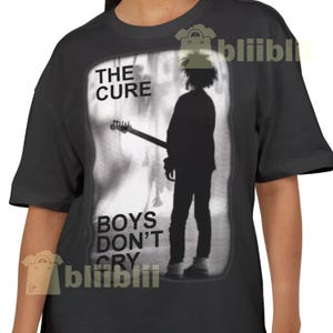 May include: Black t-shirt featuring a grayscale image of a musician with a guitar, with the text "THE CURE" above and "BOYS DON'T CRY" below. The design is rectangular and slightly blurred, creating a vintage aesthetic.