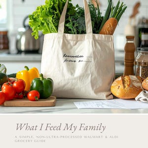 May include: A canvas tote bag filled with fresh produce, including lettuce, broccoli, and green onions. Beside the bag are tomatoes, yellow and green bell peppers, and a loaf of bread. The text on the bag reads "Remember the..." and the title below reads "What I Feed My Family".