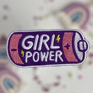 May include: Embroidered patch in the shape of a battery, featuring the words "GIRL POWER" in white. The patch has a purple background with pink and yellow accents, and a white border. The design includes a lightning bolt.