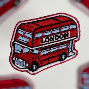 May include: Embroidered patches featuring a red double-decker bus with the word "LONDON" on the side. The patches have a white border and blue accents. The image shows multiple patches scattered on a white surface.