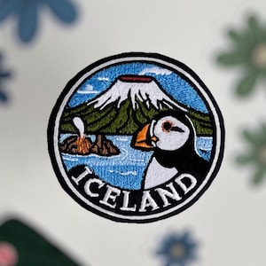 May include: A collection of embroidered patches and stickers. The central patch features a puffin, a volcano, and the word "Iceland". Other patches include green backpacks and blue and green flower designs.
