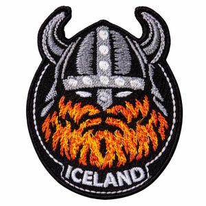 May include: Embroidered patch depicting a Viking helmet with horns, a fiery orange beard, and the word "ICELAND" in white. The patch is on a black background with white stitching around the edges.