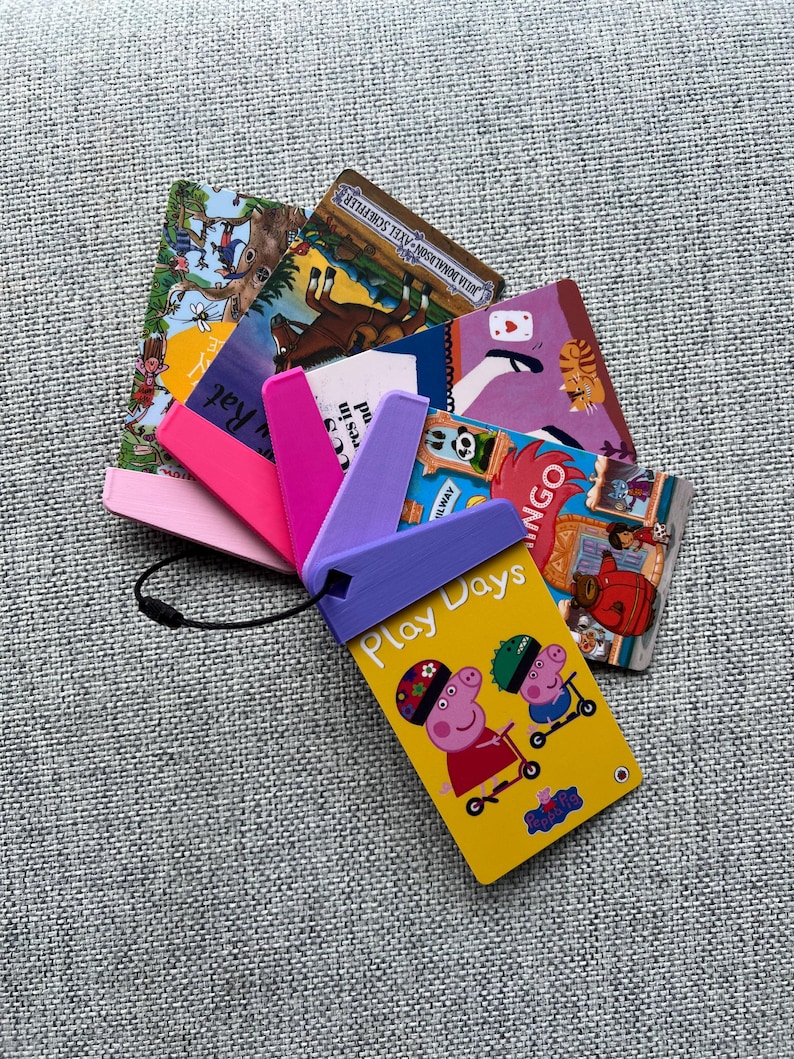 May include: A yellow card with the words "Play Days" and a picture of two cartoon pigs riding scooters. The card is attached to a purple, pink, and white plastic holder with a black string.