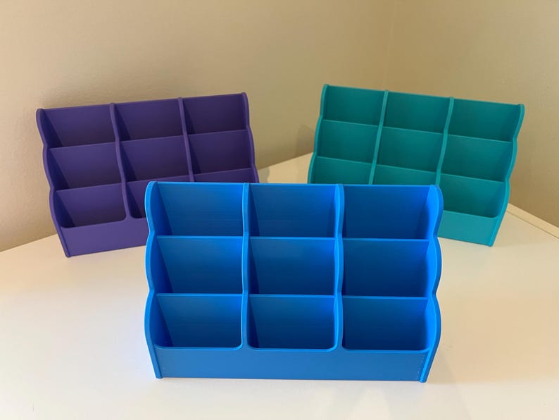 May include: Three desktop organizers with six compartments each. The organizers are made of plastic and are blue, teal, and purple.