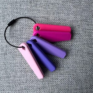 May include: A set of four keychains with a black ring. The keychains are made of a soft, flexible material and are in shades of pink and purple.