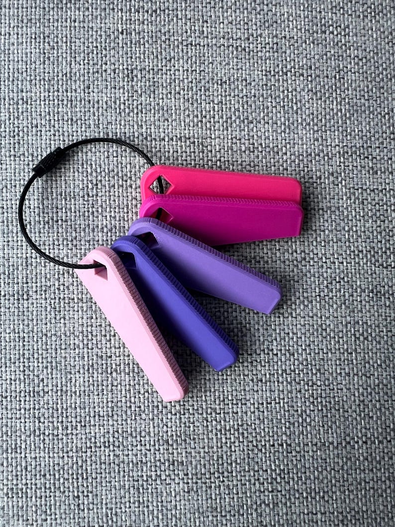 May include: A set of four keychains with a black ring. The keychains are made of a soft, flexible material and are in shades of pink and purple.