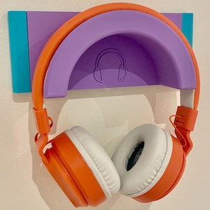 May include: A purple and orange headphone holder mounted on a wall. The holder has a curved design to hold headphones. The headphones are orange and white.
