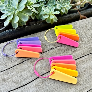 May include: A set of colorful plant markers with a rainbow color scheme. The markers are made of plastic and have a triangular shape. They are attached to a metal ring.