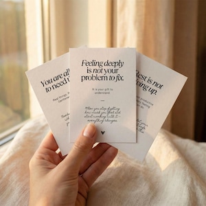 May include: A hand holds three white cards with black text. The cards feature inspirational quotes. One card says "Feeling deeply is not your problem to fix." Another says "You are all to need." The third card says "Rest is not giving up."
