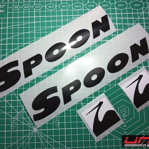 May include: Two black vinyl decals with the word "SPOON" in a bold, stylized font. A smaller black vinyl decal with a stylized bird design is also included.
