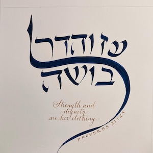 May include: A white paper print featuring dark blue Hebrew calligraphy at the top. Below the Hebrew text, the English phrase "Strength and dignity are her clothing" is written in a brown cursive script, followed by "PROVERBS 31:25".
