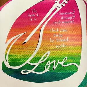 May include: A colorful paper cut-out design with the text "The heart is a thousand stringed instrument that can only be tuned with Love".