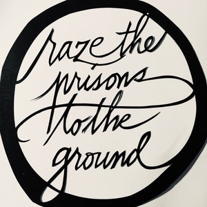 Puede incluir: Ilustración en blanco y negro de un círculo con el texto "Raze the prisons to the ground" escrito en una fuente estilizada.
