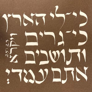 May include: A close-up of a handwritten Hebrew text on a brown background. The text is in white and is written in a cursive style. The text reads "25:23" and then continues with a longer passage of Hebrew text.