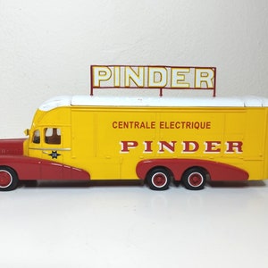 Peut inclure: Un camion jouet jaune et rouge avec le mot "PINDER" sur le dessus et le côté. Le camion a un toit blanc et les mots "CENTRALE ELECTRIQUE PINDER" sont imprimés sur le côté. Le camion a des roues rouges et un avant rouge.