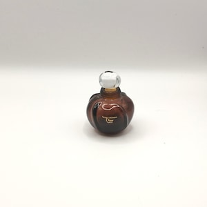 May include: A brown glass bottle of Diorissimo perfume with a white cap. The bottle has a curved shape and the text "Diorissimo Dior Paris" is printed on the front.