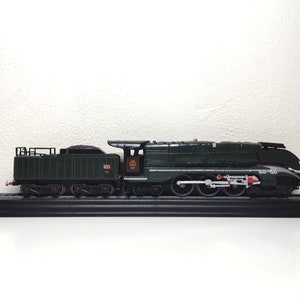 May include: A green model train locomotive with black wheels and red accents. The train is on a black display base.