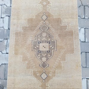 Może przedstawiać: Wietrzący kremowy dywan z brązowym geometrycznym wzorem. Dywan ma postarzony wygląd i idealnie nadaje się do dodania odrobiny stylu boho do domu.