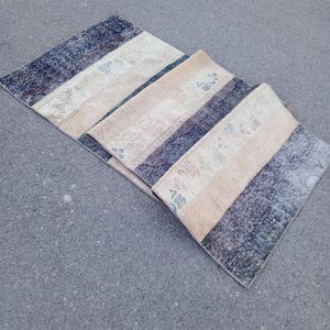 May include: Three rectangular, vintage-style rugs with a patchwork design. The rugs feature alternating stripes of faded blue, beige, and patterned sections. The rugs are arranged on a gray surface.