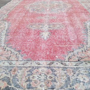 May include: A rectangular, distressed red rug with a central medallion design. The rug features a faded, vintage aesthetic with intricate border patterns in shades of blue, beige, and pink. The rug's dimensions are not visible.