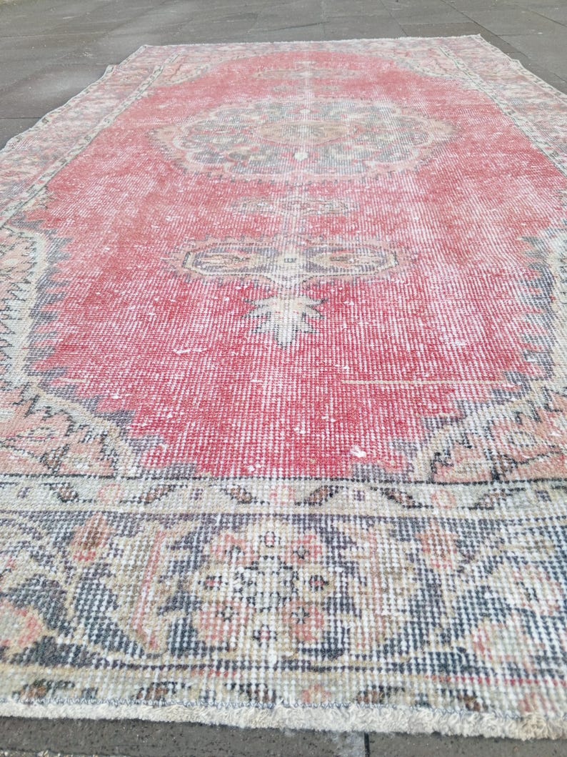 May include: A rectangular, distressed red rug with a central medallion design. The rug features a faded, vintage aesthetic with intricate border patterns in shades of blue, beige, and pink. The rug's dimensions are not visible.