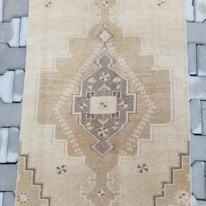 Może przedstawiać: Dywan w stylu vintage z beżowym tłem i brązowym geometrycznym wzorem. Dywan ma frędzlowane brzegi.