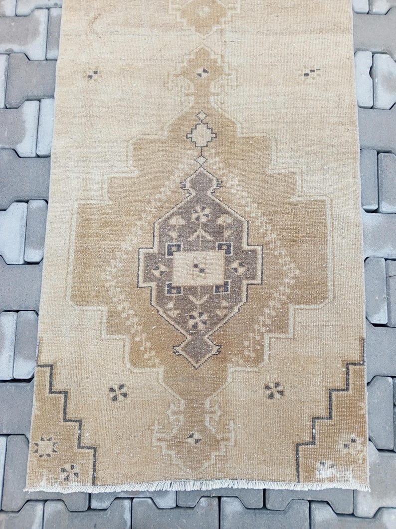 Może przedstawiać: Dywan w stylu vintage z beżowym tłem i brązowym geometrycznym wzorem. Dywan ma frędzlowane brzegi.
