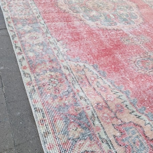 May include: A distressed, rectangular rug with a faded red central field and a detailed, patterned border. The rug features a central medallion design in muted tones of blue, beige, and peach. The overall aesthetic is vintage and well-worn.
