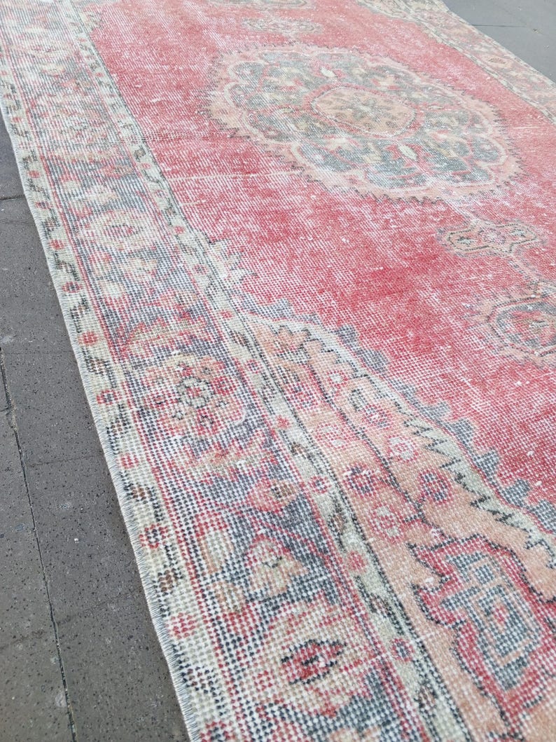 May include: A distressed, rectangular rug with a faded red central field and a detailed, patterned border. The rug features a central medallion design in muted tones of blue, beige, and peach. The overall aesthetic is vintage and well-worn.