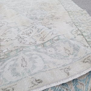 May include: A white and light blue vintage rug with a distressed look and a fringe border.