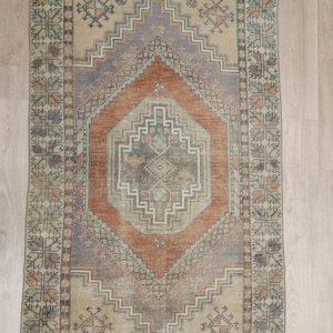 May include: A vintage rug with a geometric pattern in shades of brown, beige, and green. The rug has a central diamond shape with a smaller diamond inside. The rug has a faded look, giving it a vintage feel.