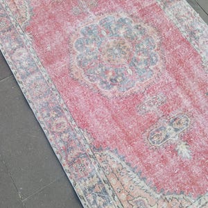 May include: A rectangular, distressed rug with a faded red central field and intricate floral patterns in blue, beige, and orange. The rug has a detailed border and a vintage aesthetic, suitable for home decor.