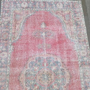 May include: A rectangular, distressed-look rug with a central red field and ornate border. The rug features a faded, vintage aesthetic with intricate floral and geometric patterns in shades of red, blue, and beige.