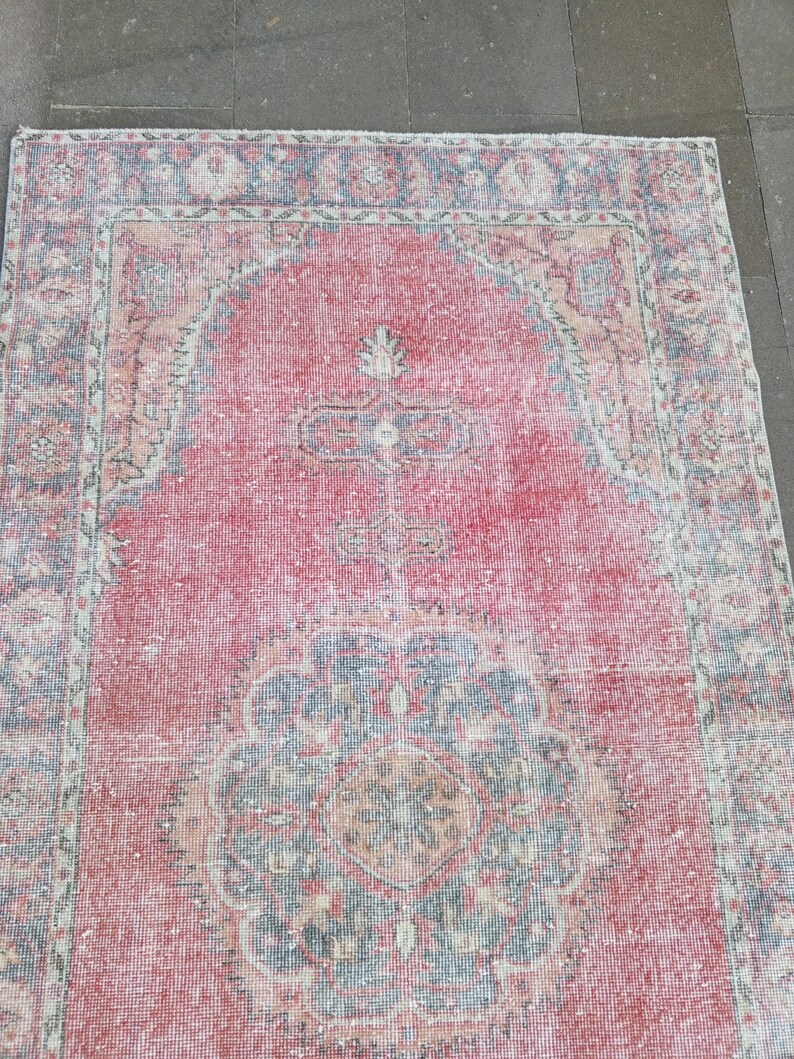 May include: A rectangular, distressed-look rug with a central red field and ornate border. The rug features a faded, vintage aesthetic with intricate floral and geometric patterns in shades of red, blue, and beige.