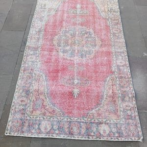May include: A rectangular, distressed rug with a faded red central field and a detailed border. The rug features a central medallion design and intricate patterns in shades of blue, green, and cream. The rug's worn appearance suggests it is vintage.