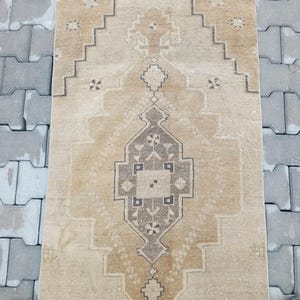 Może przedstawiać: Wietrzny dywan w kolorze beżowym i brązowym z geometrycznym wzorem. Dywan ma frędzle i jest wykonany z wełny.