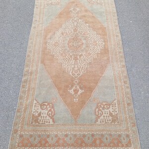 May include: A vintage rug with a light brown and beige color scheme. The rug has a central diamond-shaped medallion with intricate floral patterns. The rug has a border with a repeating pattern of small floral motifs.