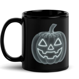 May include: Black ceramic mug featuring a glowing neon-style jack-o'-lantern design. The pumpkin has a stitched top and triangular eyes and mouth. A perfect Halloween-themed gift for coffee or tea lovers.