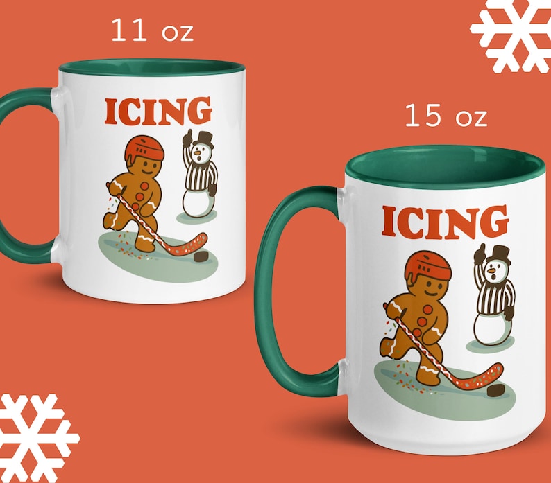 May include: Two white ceramic mugs with green handles and rims. The mugs feature a gingerbread man playing hockey with the word "ICING" in orange. One mug is 11 oz, the other is 15 oz.