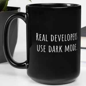 May include: Black ceramic coffee mug with white text that reads "REAL DEVELOPERS USE DARK MODE."