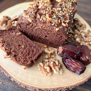 May include: A loaf of chocolate banana bread topped with chopped walnuts, sliced and served on a wooden platter with dates and walnuts.