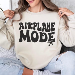 May include: A sand colored sweatshirt with the text "AIRPLANE MODE" in black retro font. A small airplane graphic is below the text.