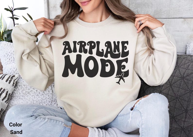 May include: A sand colored sweatshirt with the text "AIRPLANE MODE" in black retro font. A small airplane graphic is below the text.
