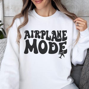May include: White sweatshirt with black text that reads "AIRPLANE MODE" in a retro font. A small airplane icon is below the text.