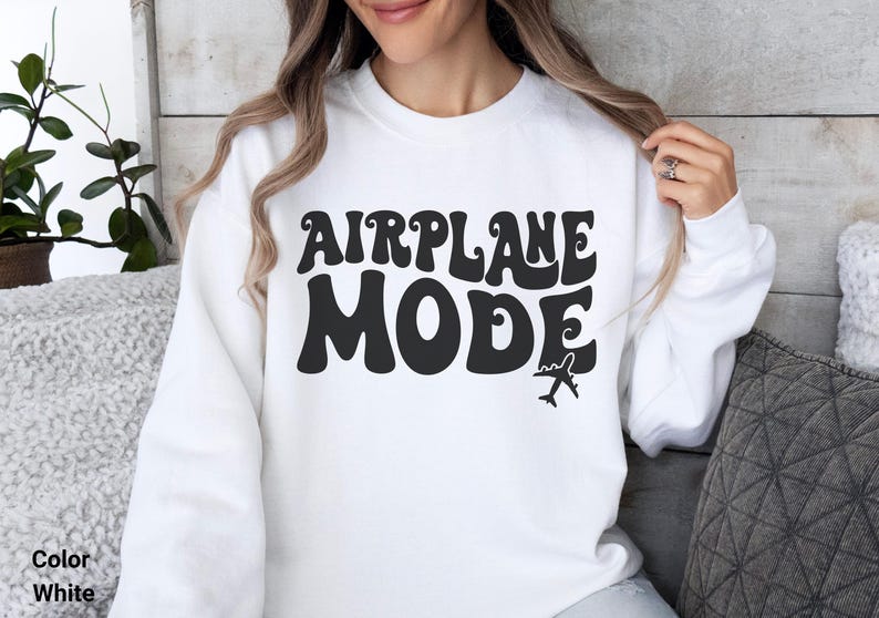 May include: White sweatshirt with black text that reads "AIRPLANE MODE" in a retro font. A small airplane icon is below the text.