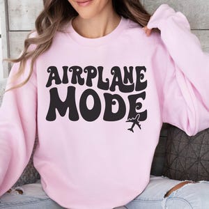 May include: A light pink sweatshirt with the text "AIRPLANE MODE" in black retro font. A small airplane icon is below the text.