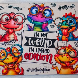 May include: A rectangular mouse mat with cartoon dinosaurs wearing glasses in different colours. The mat has the text "I'M NOT WEIRD I'M LIMITED EDITION" and hashtags such as #adorable, #unique, and #limitededition.